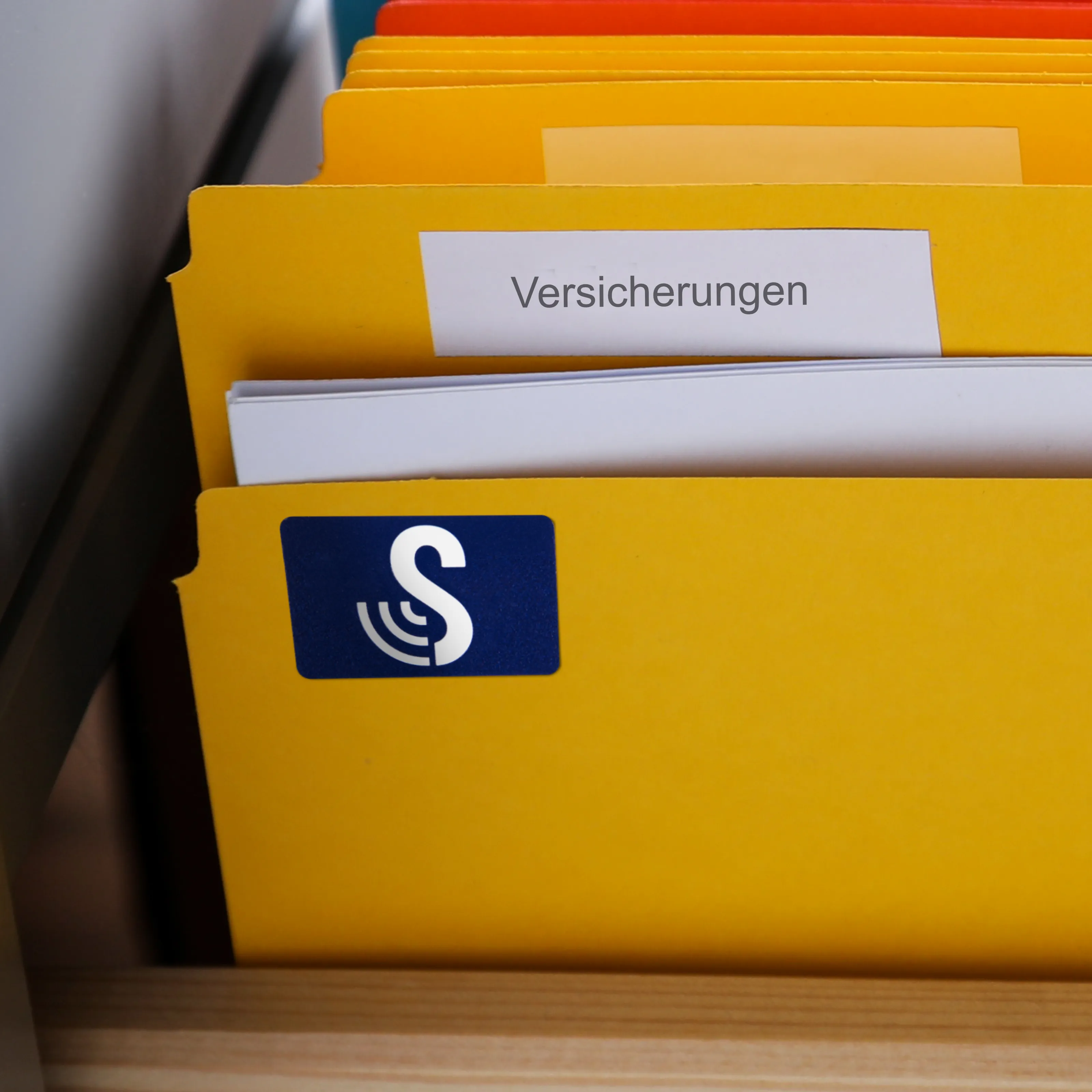 Ein gelbes Aktenheft trägt die Aufschrift Versicherungen. Darauf befindet sich ein großer Standard SenseTap Sticker.