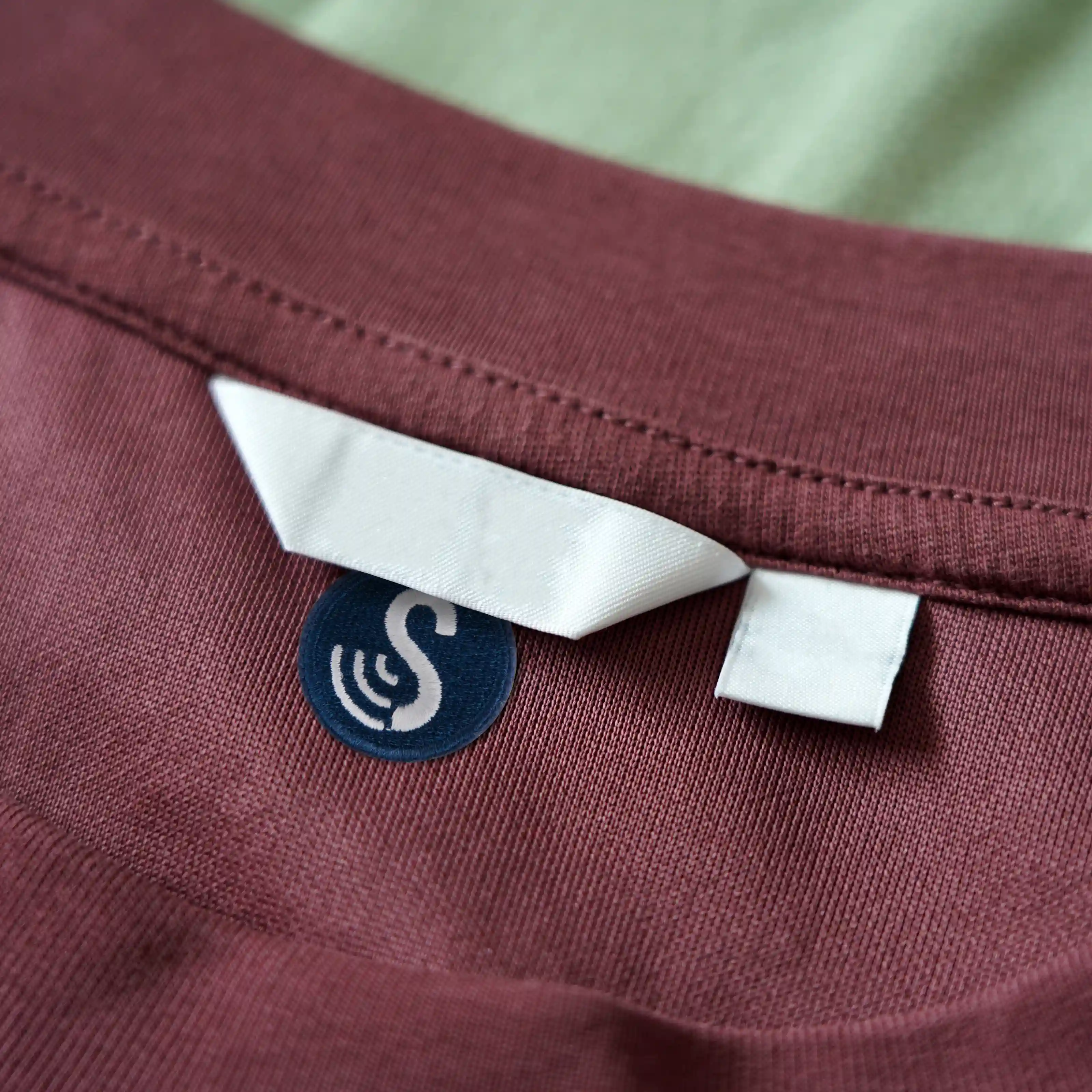 A dark blue, iron-on SenseTap laundry tag is placed underneath the brand label of a top. The SenseTap logo is featured on the tag.