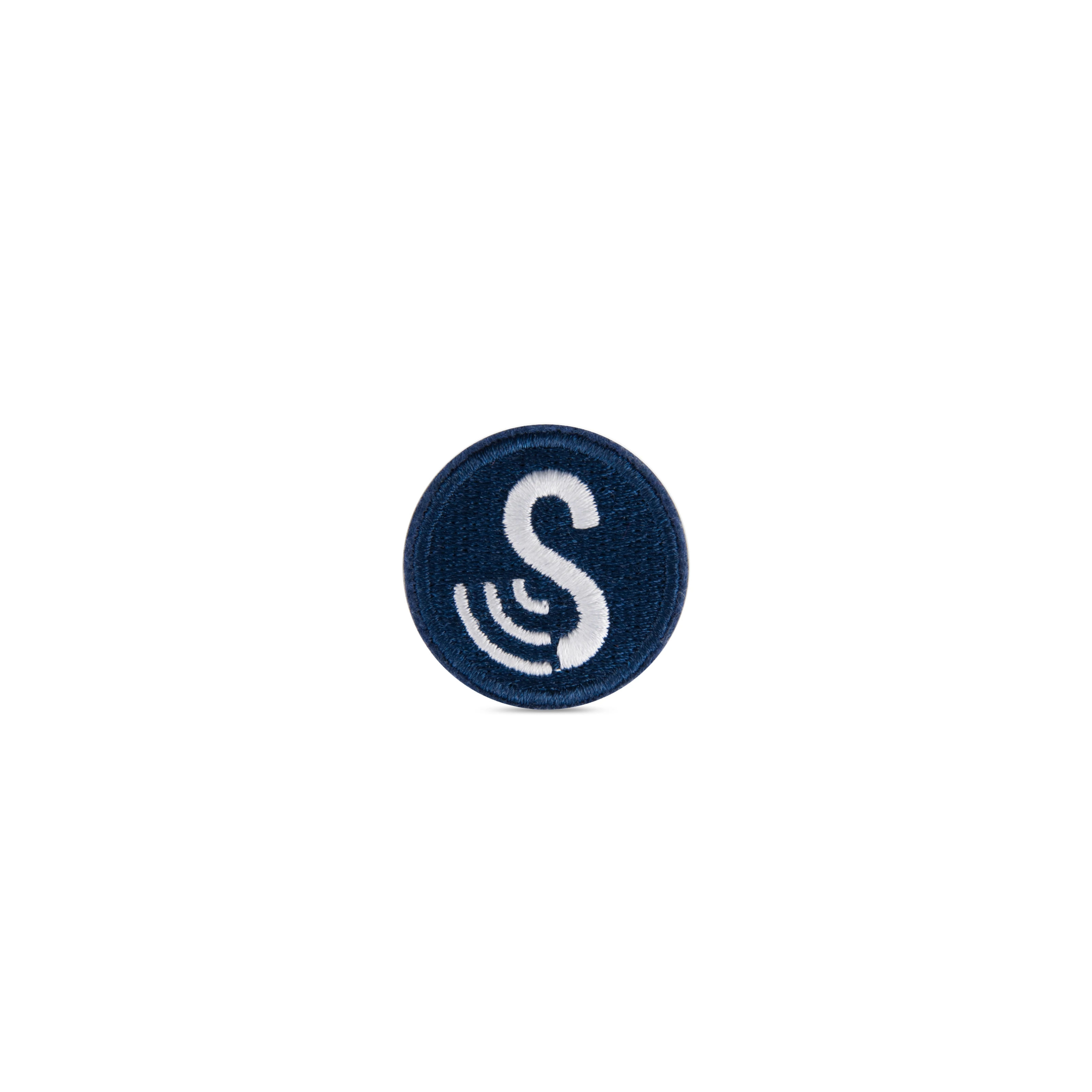 Front view of the round, iron-on SenseTap laundry tag. The tag has a diameter of 30 mm and is dark blue. The embroidered SenseTap logo is featured on the tag and consists of a large white S with three curved lines extending to the left.