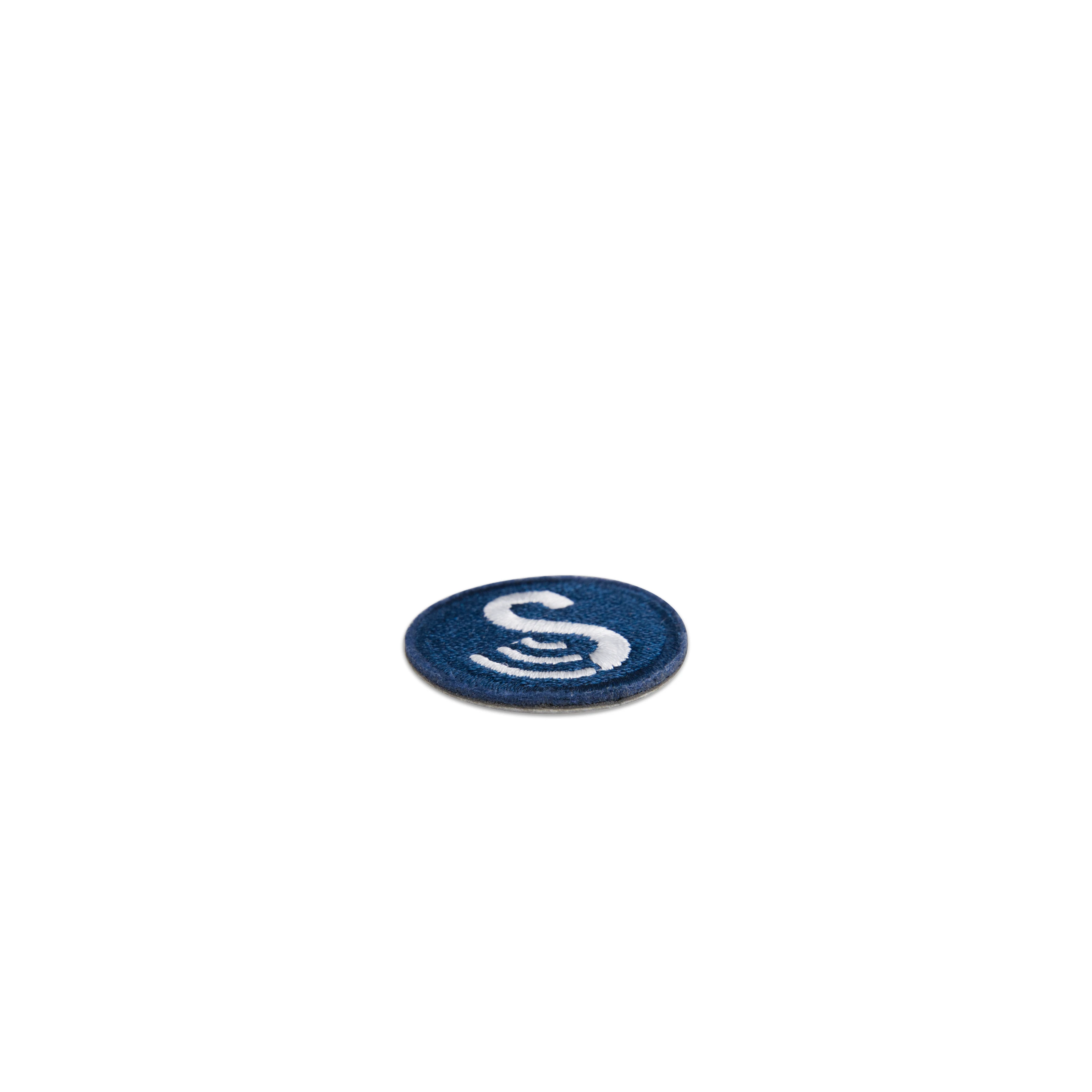 Side view of the round, iron-on SenseTap laundry tag. The tag has a diameter of 30 mm and is dark blue. The embroidered SenseTap logo is featured on the tag and consists of a large white S with three curved lines extending to the left.